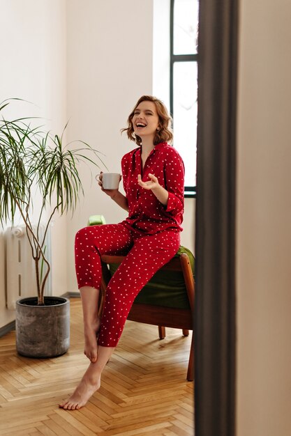 Opgewonden blootsvoets vrouw in pyjama met kopje koffie. Volle lengte weergave van vrolijke vrouw thee drinken en thuis glimlachen.