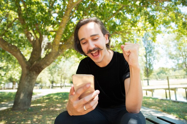 Opgewonden dolblij man met smartphone verheugt zich over goed nieuws