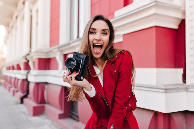 Opgewonden donkerharige meisje in een rode jas met plezier met camera
