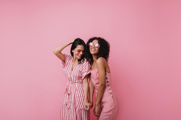 Opgewonden europees meisje speelt met haar haar tijdens fotoshoot met vriend studioportret van vrolijke dames in roze kleding