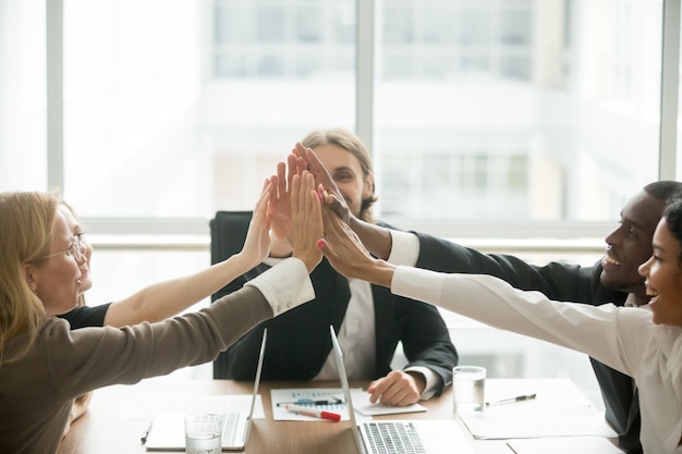 Opgewonden gelukkig multiraciaal commercieel team dat high-five geeft op kantoorvergadering