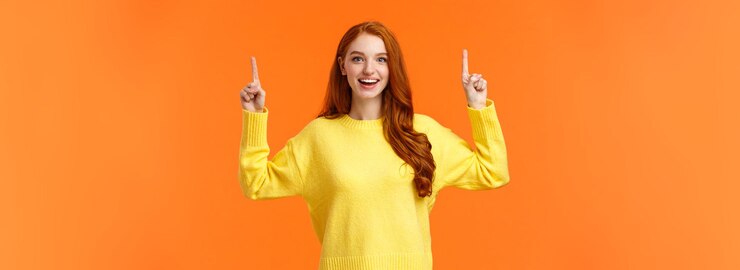 Gratis Foto opgewonden, goed uitziende roodharige meid met sproeten draagt een gele trui die naar boven wijst en jo glimlacht