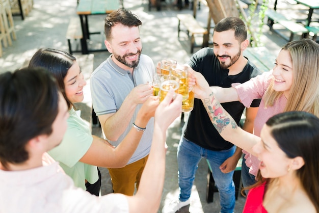 Opgewonden groep vrienden van in de twintig die een toast uitbrengen met bier en lachen. Aantrekkelijke vrienden die rondhangen tijdens hun vriendschapsreünie