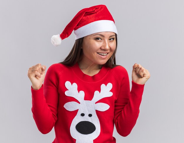 Gratis foto opgewonden jong aziatisch meisje dat kerstmishoed met sweater draagt die ja gebaar toont dat op witte achtergrond wordt geïsoleerd