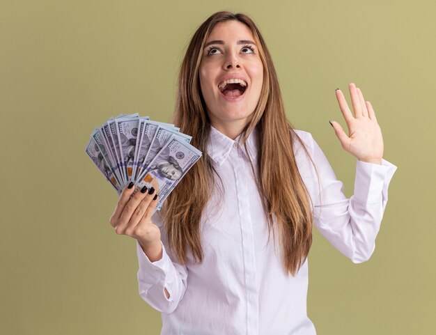 Opgewonden jong mooi blank meisje staat met opgeheven hand en houdt geld omhoog kijkend