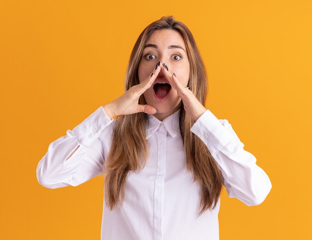 Opgewonden jong, vrij blank meisje houdt handen dicht bij de mond geïsoleerd op een oranje muur met kopieerruimte