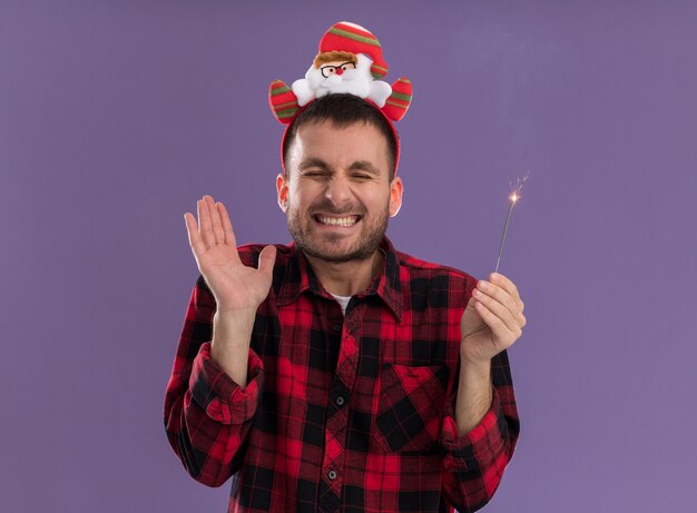 Gratis foto opgewonden jonge blanke man met hoofdband van de kerstman met vakantie sterretje met lege hand lachend met gesloten ogen geïsoleerd op paarse achtergrond