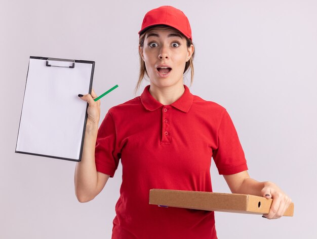 Opgewonden jonge mooie bezorger in uniform houdt klembord en pizzadoos geïsoleerd op een witte muur