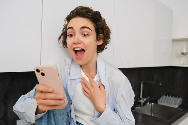Opgewonden jonge vrouw kijkt verbaasd naar mobiele telefoon scherm chats met iemand ziet verbazingwekkend nieuws op sm