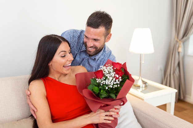 Opgewonden jonge vrouw ontvangt onverwacht boeket rode rozen van echtgenoot thuis valentijnsdag