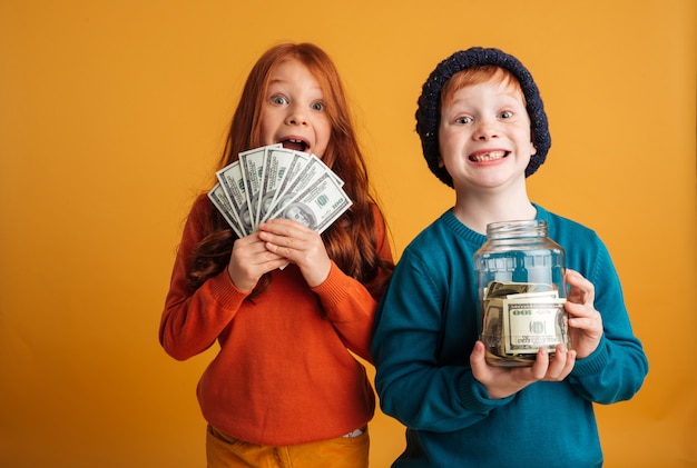 Opgewonden kleine roodharige kinderen die geld aanhouden.