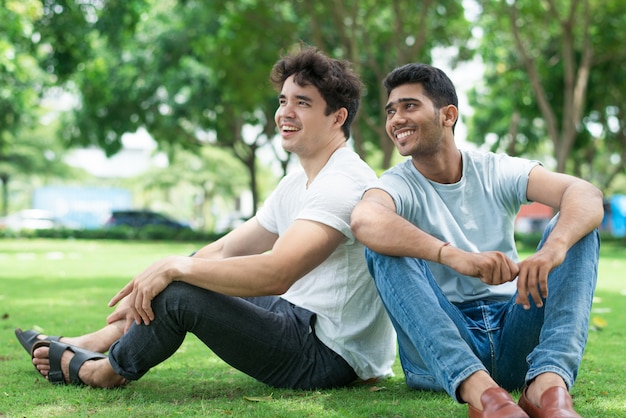Opgewonden knappe jonge mannen in casual kleding zittend op het gras
