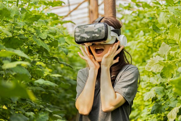 Opgewonden meisje dat VR-set draagt en haar handen voor haar gezicht houdt in de kas