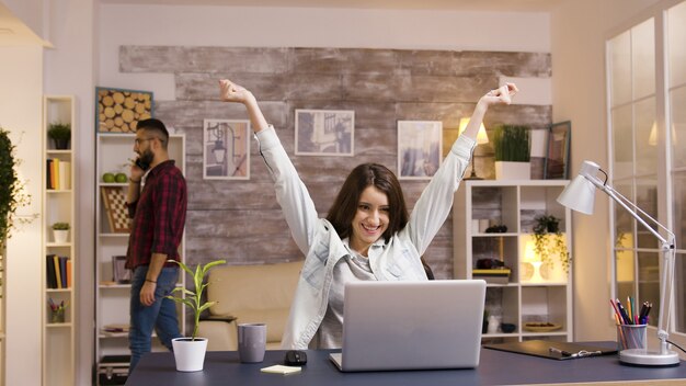 Opgewonden meisje met opgeheven handen tijdens het werken op laptop in de woonkamer. Slow motion beelden