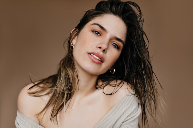Opgewonden meisje met trendy make-up. Indoor foto van elegante zwartharige vrouw poseren met zachtjes glimlach.