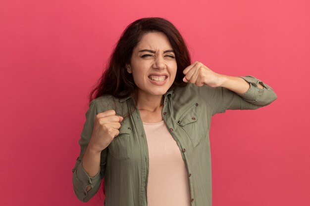 Opgewonden met gesloten ogen jong mooi meisje dat olijfgroen t-shirt draagt dat ja gebaar toont dat op roze muur wordt geïsoleerd