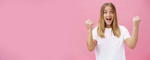 Opgewonden vrolijke en optimistische charmante vrouw met blond haar in een wit t-shirt die vuisten opsteekt in victo