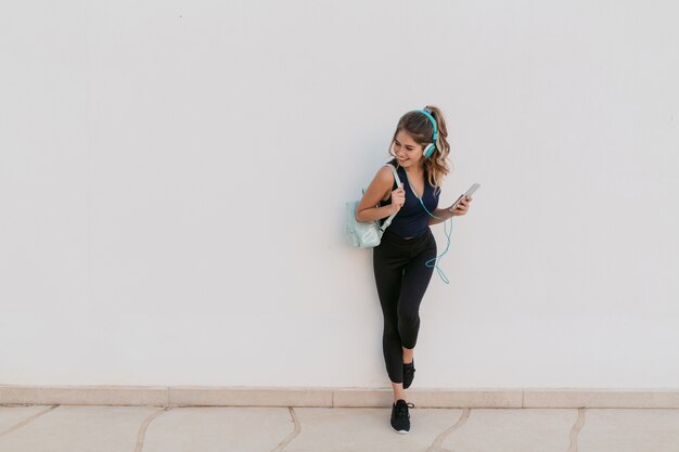 Opgewonden vrolijke jonge vrouw in sportkleding, luisteren naar muziek via een koptelefoon. Glimlachen naar de andere kant, positiviteit, ware emoties, gezonde levensstijl, fitness uitdrukken.