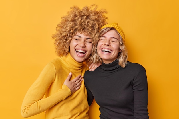 Oprechte menselijke emoties concept Positieve dolblij jonge vrouwen hebben plezier lachen graag glimlach tanden kan niet stoppen met lachen staan dicht bij elkaar gekleed terloops geïsoleerd over gele muur