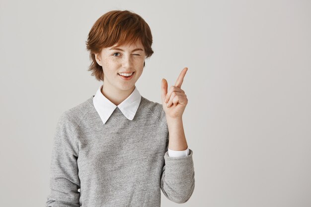 Optimistisch roodharig meisje met kort kapsel poseren tegen de witte muur