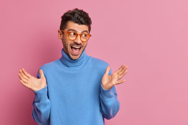 Optimistische hipster-man steekt zijn handpalmen op en reageert op geweldig nieuws