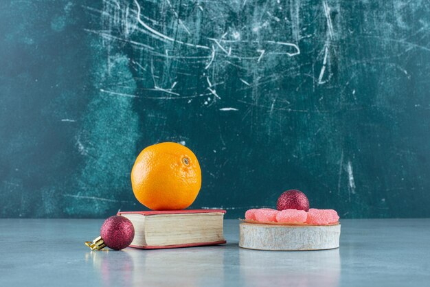 Orange op een boek, marmelade op een houten stuk en twee decoratieve ballen op marmer.