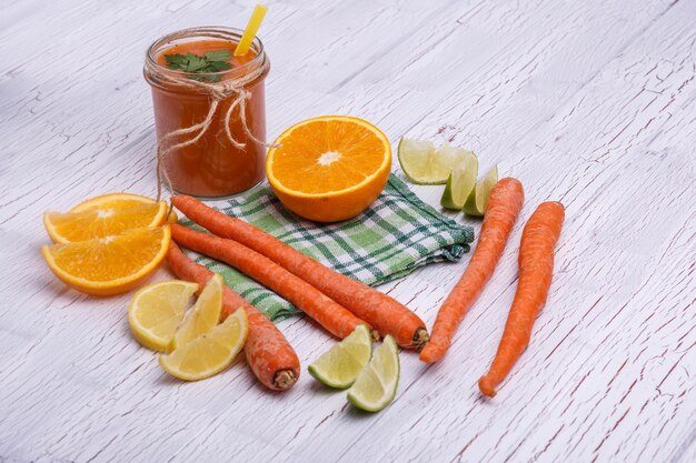 Oranje detox cocktail met sinaasappelen en wortelen ligt op een witte tafel