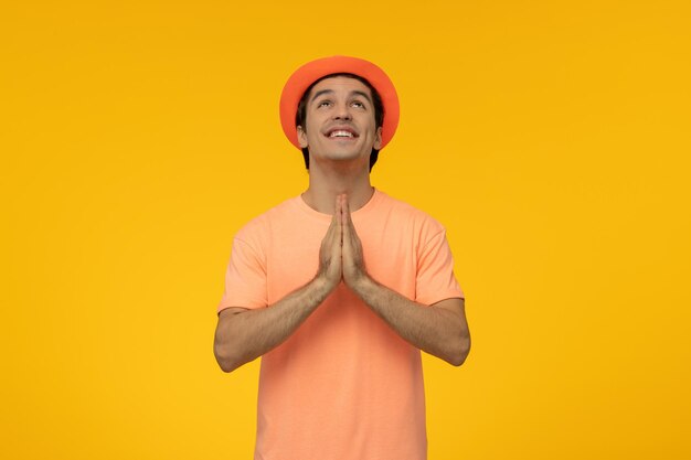 Oranje hoed gelukkige knappe mooie kerel in oranje t-shirt met de hoed die bidt en omhoog kijkt