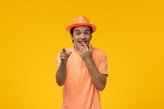 Oranje hoed schattige jonge kerel in oranje shirt met de hoed bijtende vinger en wijzend naar voren