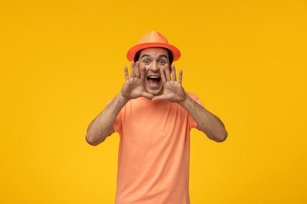 Oranje hoed, schattige jonge kerel in oranje t-shirt met de hoed die schreeuwt en handen rond de mond legt