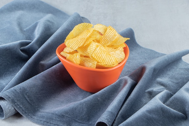 Oranje kom smakelijke rimpelchips op steen.