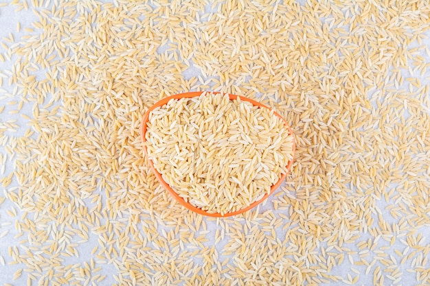 Oranje kom vol bruine rijst in het midden van verspreide korrels op een marmeren oppervlak