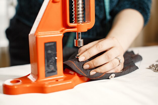 Oranje pers voor kleding. Knopen op stof. Vrouw met naaiende hulpmiddelen