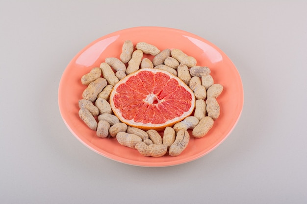 Oranje plaat van grapefruit slice en biologische pinda's op witte achtergrond. Hoge kwaliteit foto
