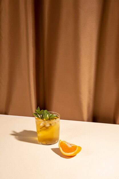 Oranje plak en cocktaildrankglas op witte lijst dichtbij bruin gordijn
