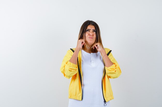 Ortrait van vrouwelijke inpluggen oren met vingers in t-shirt, jas en op zoek geërgerd vooraanzicht