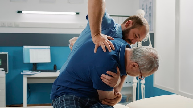 Osteopaat helpt senior man om botten in de kast te kraken, fysiotherapieoefening te doen. Mannelijke assistent die fysiotherapieprocedure gebruikt om de mobiliteit te vergroten en de patiënt te behandelen.