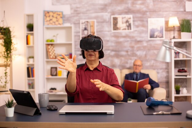 Oude bejaarde vrouw gebruikt voor het eerst een VR virtual reality-headset in haar huis. Concept van actieve ouderen die moderne technologie gebruiken