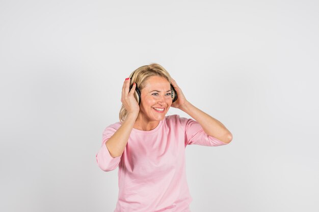 Oude glimlachende vrouw in roze blouse met hoofdtelefoons