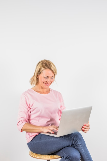 Oude glimlachende vrouw in roze blouse met laptop op kruk