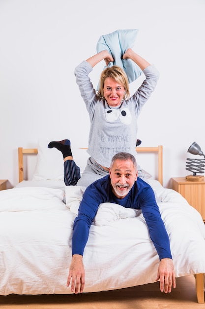 Oude glimlachende vrouw met hoofdkussen en de mens die op bed liggen