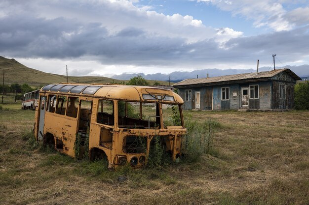 Oude kapotte bus op een veld door een huis gevangen in Armenië