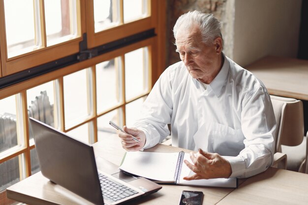 Oude man aan de tafel zitten en werken met een laptop