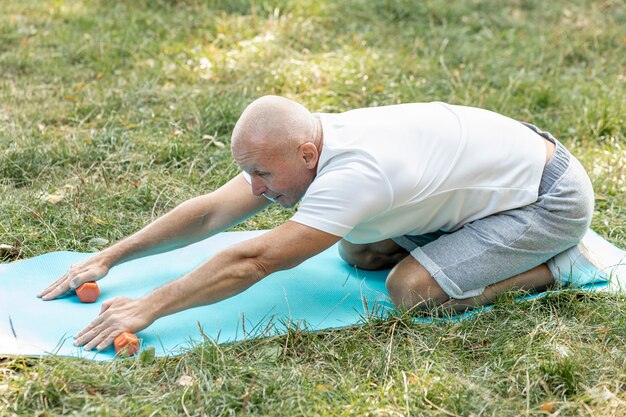 Oude man die zich uitstrekt over yoga mat