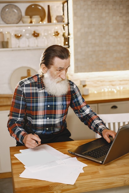 Oude man met laptop. Grootvader zit in een kerstversiering. Man in een celoverhemd.