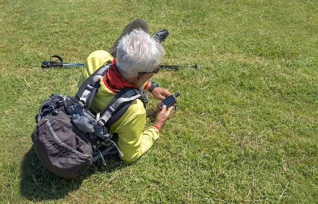 Oude mannelijke wandelaar liggend op een weide en kijken naar handheld navigator