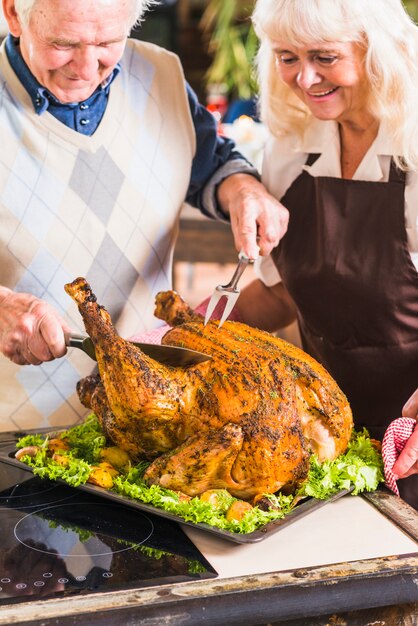 Oude mens die geroosterde ham dichtbij vrouw snijdt