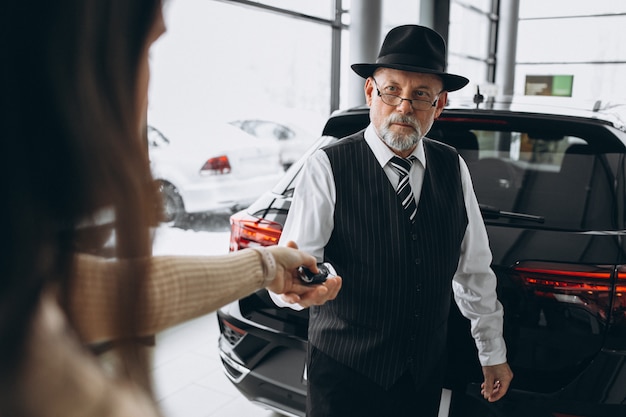 Oude mens die sleutels van auto in een autotoonzaal ontvangt