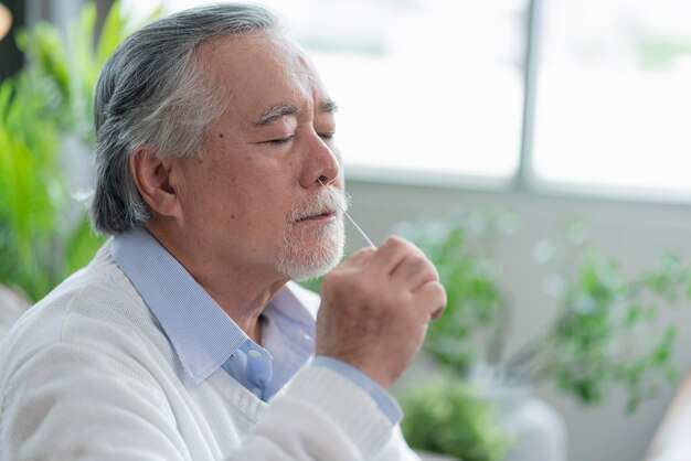 Oude senior aziatische mannenhand neusuitstrijkje die zelf snelle tests test voor detectie van het SARS-co2-virus thuis isoleren quarantaineconcept