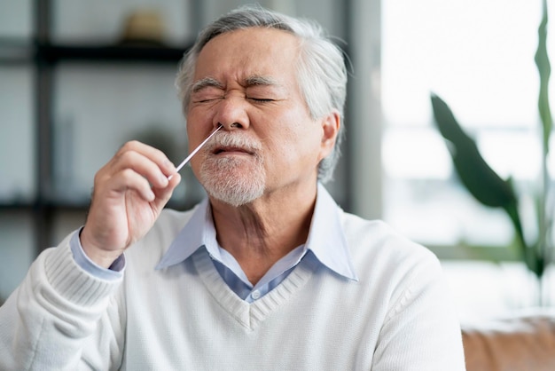 Oude senior aziatische mannenhand neusuitstrijkje die zelf snelle tests test voor detectie van het SARS-co2-virus thuis isoleren quarantaineconcept